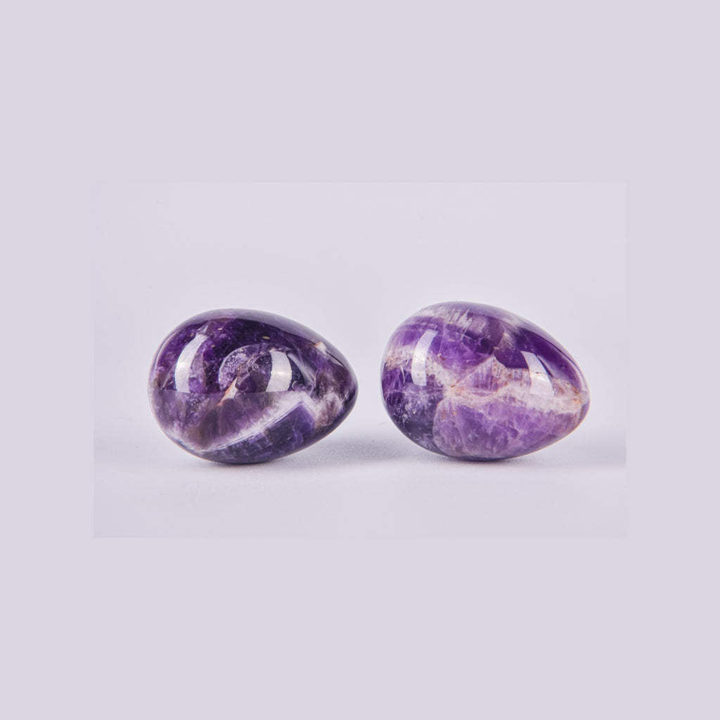 Pareja de piedras huevo de Amatista mostrando las variaciones naturales del mineral, con posibles vetas de cuarzo y distintos tonos de violeta.