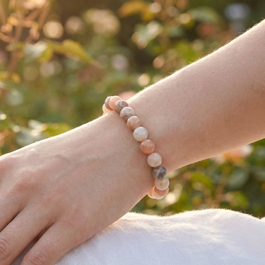 Mujer luciendo pulsera de Piedra Luna multicolor en la muñeca bajo la luz del sol. Amuleto de Adularia para conectar con la feminidad y la calma interior.