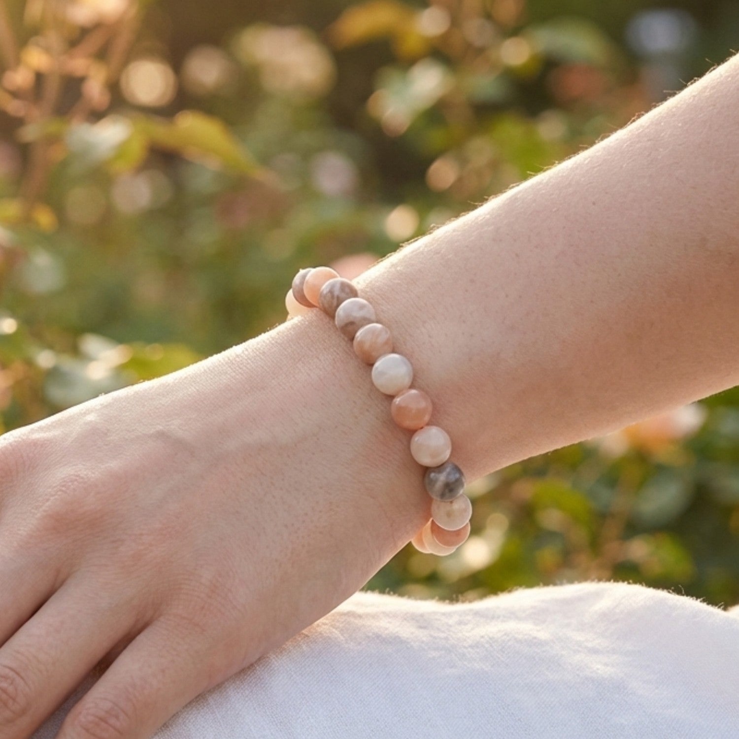 Mujer luciendo pulsera de Piedra Luna multicolor en la muñeca bajo la luz del sol. Amuleto de Adularia para conectar con la feminidad y la calma interior.