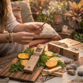 Ritual al aire libre con Pack de Inciensos Naturales Sagrada Madre. Manos encendiendo una varilla junto a cajas de Copal y Citronella con Naranja y Palo Santo sobre mesa de madera.