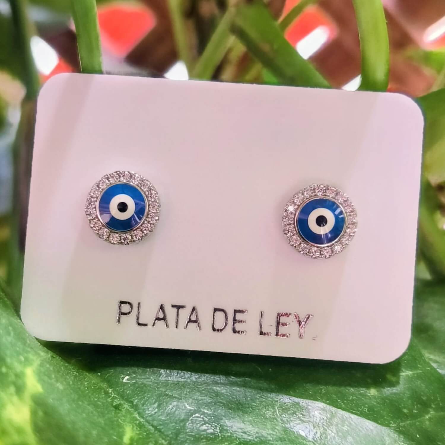Pendientes ojo turco plata 925 con circonitas, fotografiados entre hojas verdes