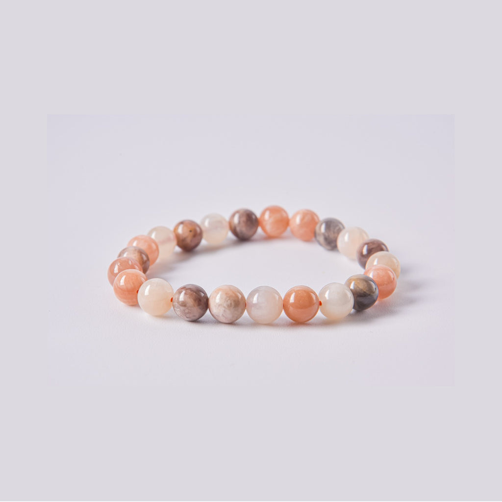 Pulsera elástica de bolas de Piedra Luna (Adularia) variedad oscura y melocotón. Detalle de las vetas naturales y el brillo del mineral sobre fondo blanco.