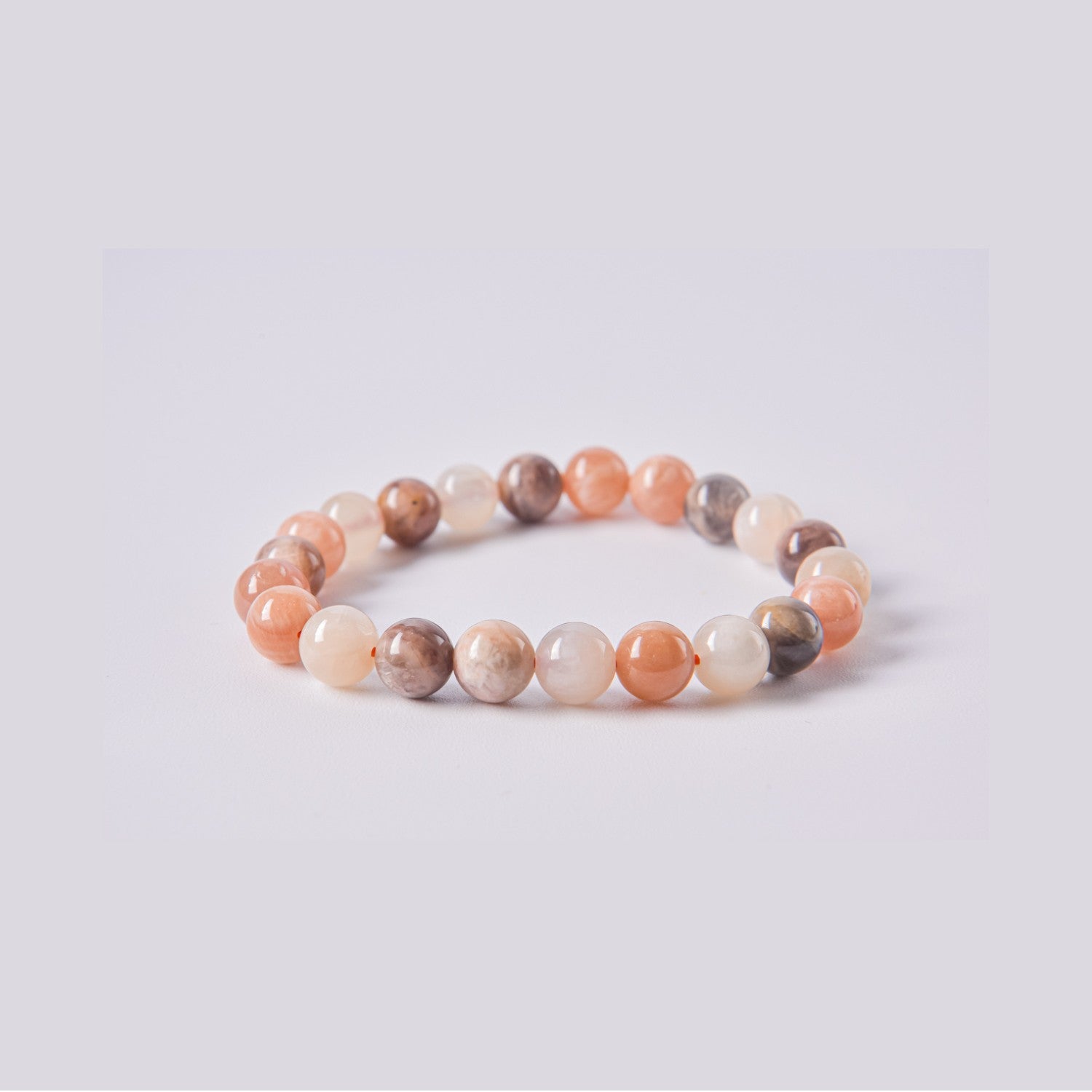 Pulsera elástica de bolas de Piedra Luna (Adularia) variedad oscura y melocotón. Detalle de las vetas naturales y el brillo del mineral sobre fondo blanco.