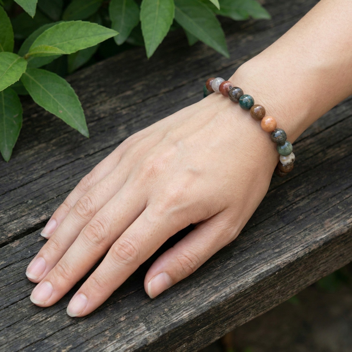 Pulsera de cuentas de Ágata India multicolor en muñeca sobre fondo de madera natural. Joyería de piedra semipreciosa en tonos tierra y verde. Colección Aura Plena