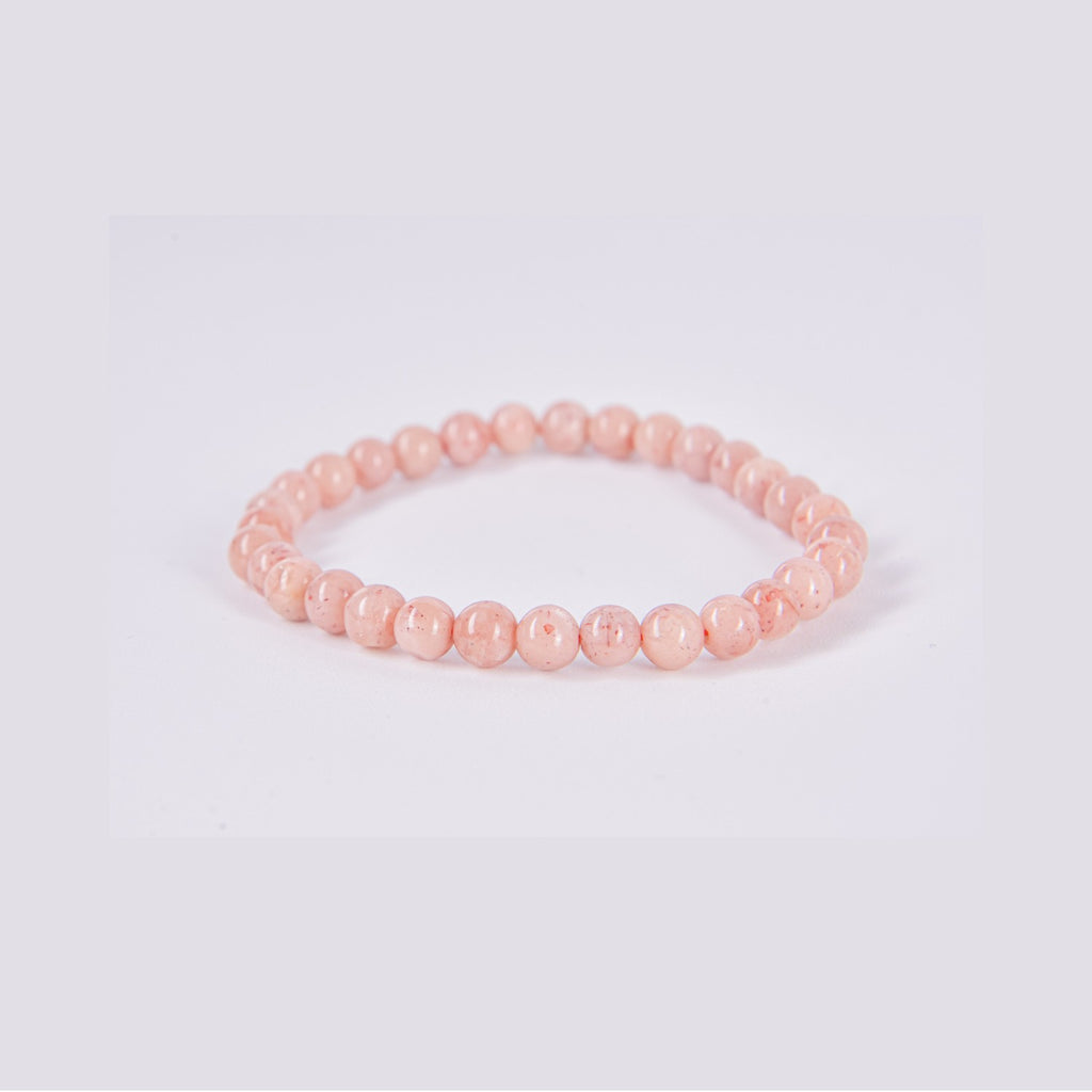 Pulsera elástica de bolas redondas de Piedra Sol natural sobre fondo blanco. Detalle del color naranja melocotón y las inclusiones brillantes típicas del mineral.