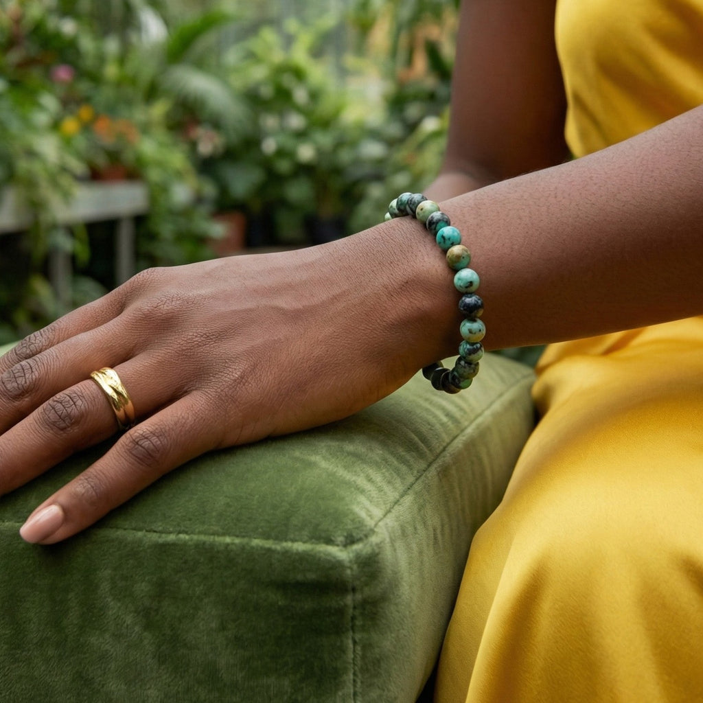 Mujer luciendo pulsera de Jaspe Turquesa Africana sobre un cojín de terciopelo verde. Joyería natural elegante que simboliza la evolución y el cambio positivo.