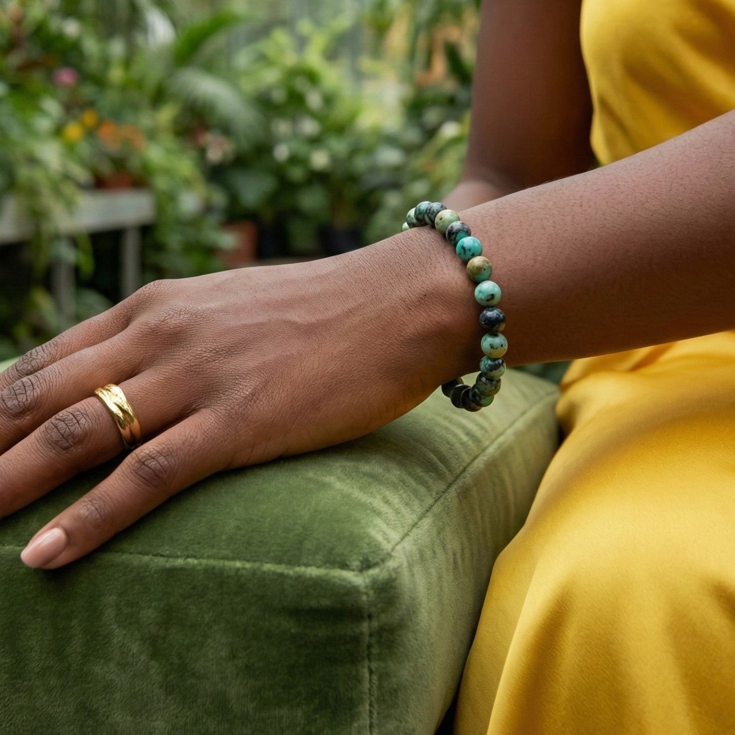 Mujer luciendo pulsera de Jaspe Turquesa Africana sobre un cojín de terciopelo verde. Joyería natural elegante que simboliza la evolución y el cambio positivo.