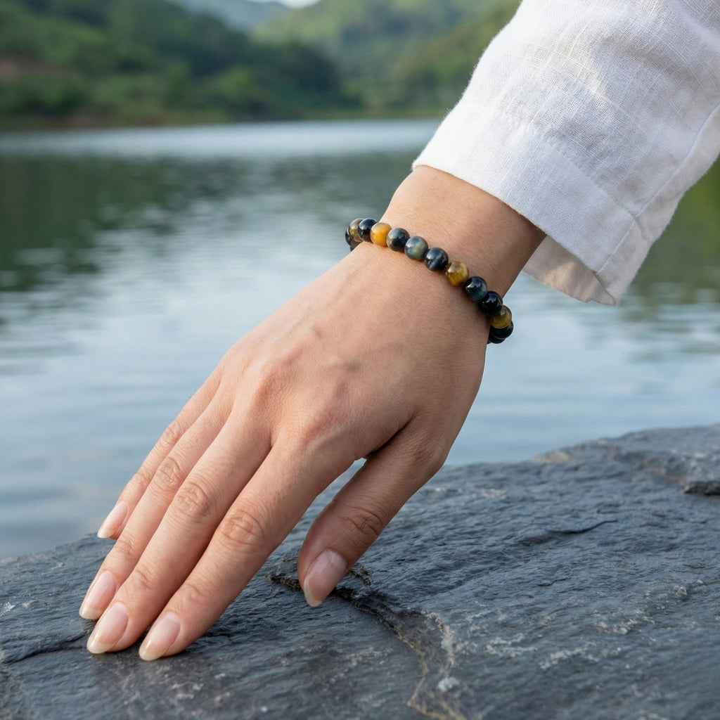 Pulsera de Ojo de Halcón (Ojo de Tigre Azul) en la muñeca con un lago de fondo. Piedra natural con destellos azulados para potenciar la intuición y la claridad mental.