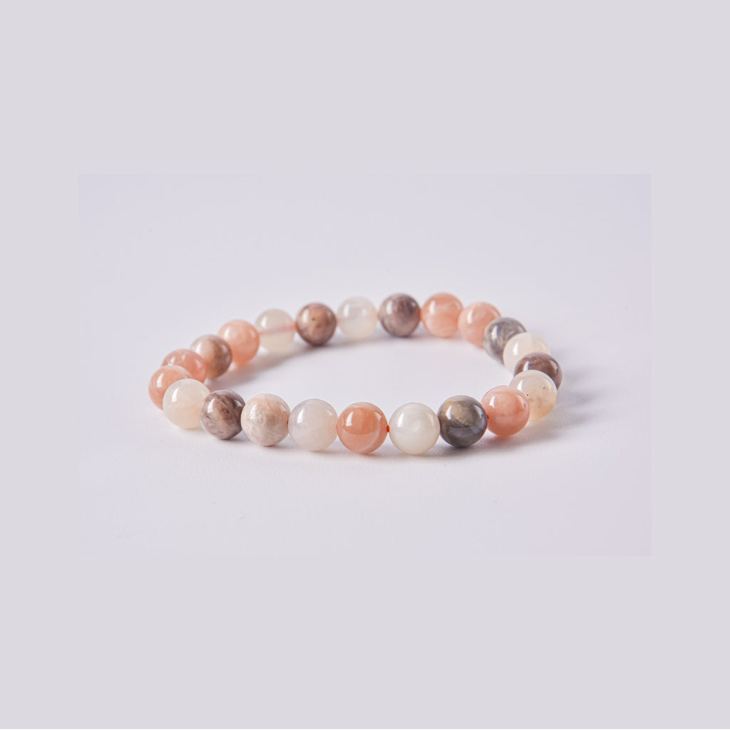 Pulsera de cuentas de Piedra Luna (Adularia) natural en tonos melocotón, crema y gris sobre fondo blanco. Joyería energética para la ansiedad y el equilibrio.