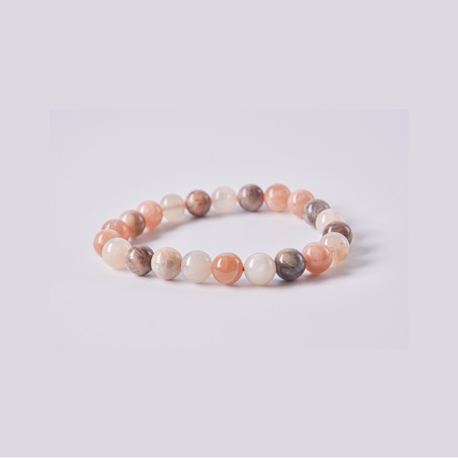 Pulsera de cuentas de Piedra Luna (Adularia) natural en tonos melocotón, crema y gris sobre fondo blanco. Joyería energética para la ansiedad y el equilibrio.