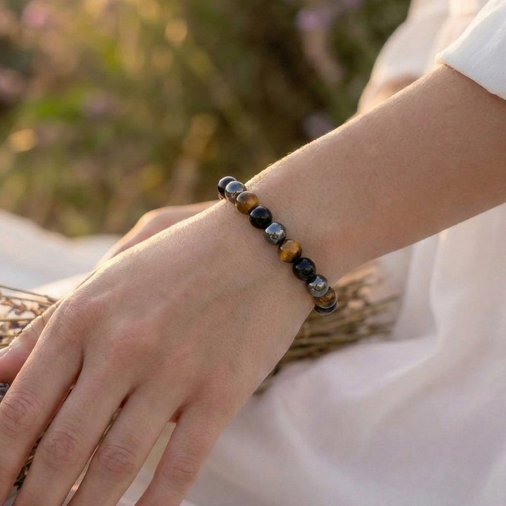 Mujer llevando la Pulsera de Triple Protección bajo luz natural. Amuleto energético con cuentas de Ojo de Tigre (suerte), Hematita (equilibrio) y Obsidiana Negra (protección contra energías negativas).