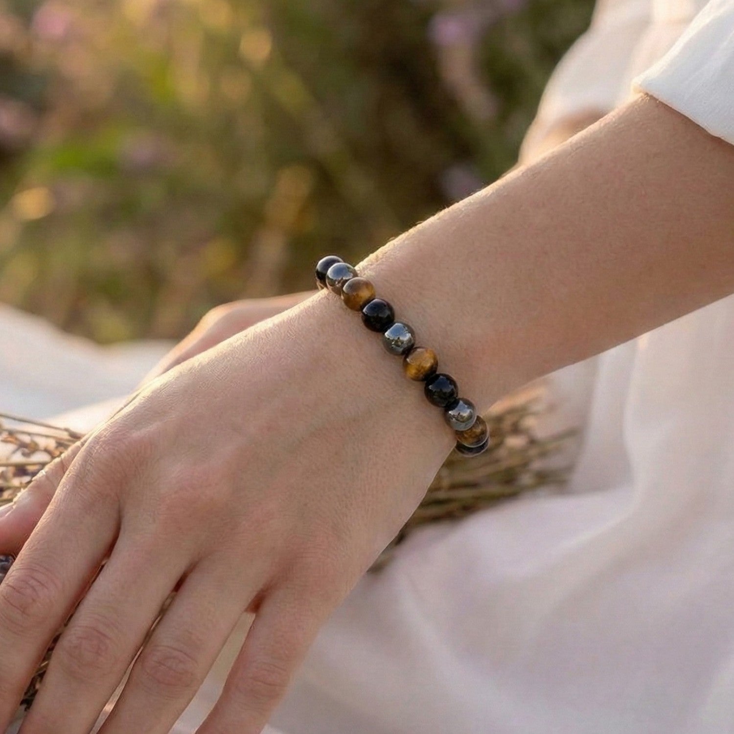 Mujer llevando la Pulsera de Triple Protección bajo luz natural. Amuleto energético con cuentas de Ojo de Tigre (suerte), Hematita (equilibrio) y Obsidiana Negra (protección contra energías negativas).