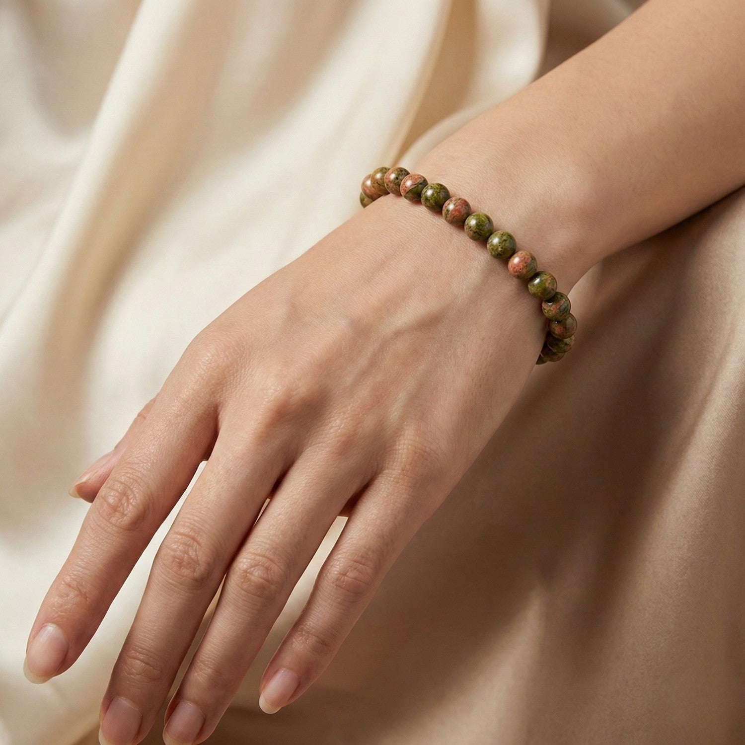 Pulsera elástica de Unakita natural con patrón moteado verde musgo y rosa salmón. Joyería para la sanación emocional y el renacimiento.