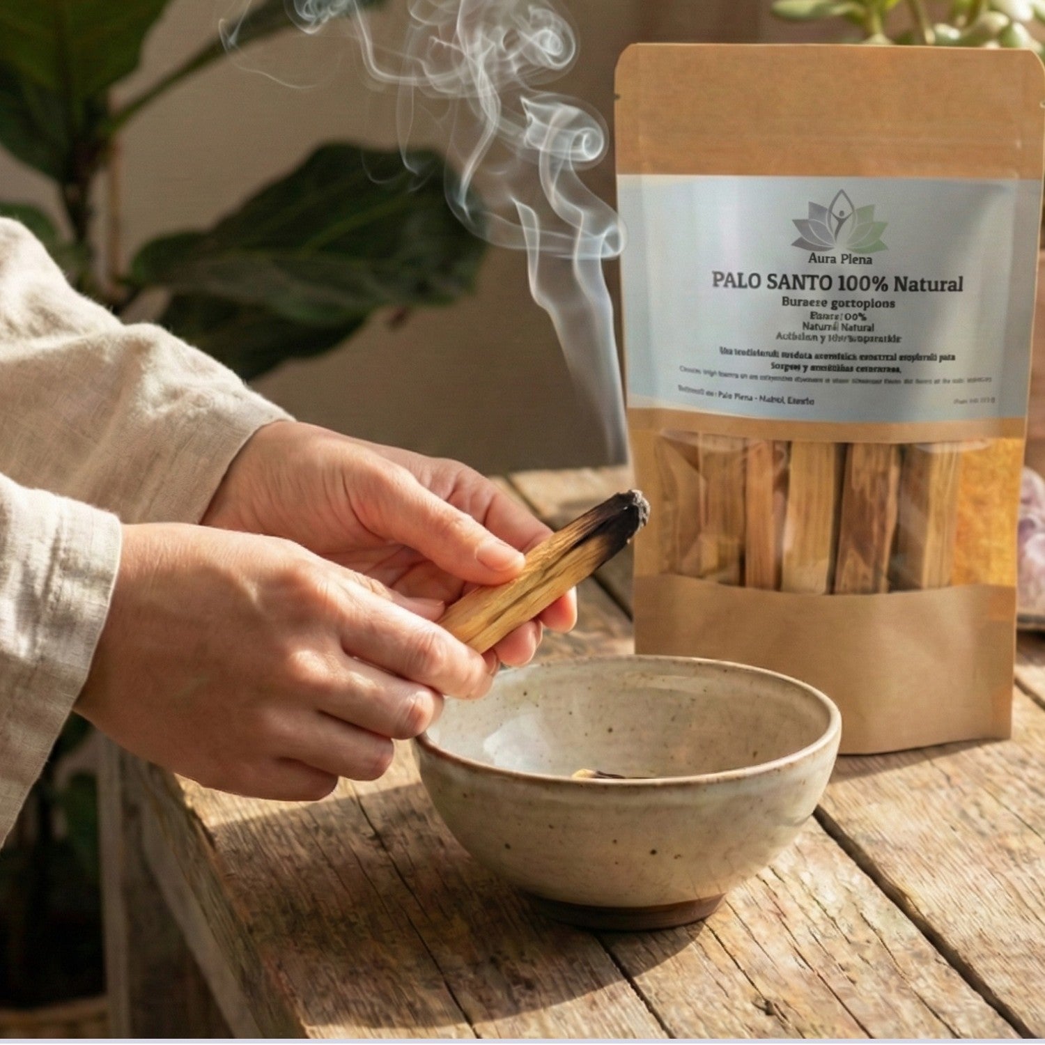 Manos realizando un ritual de limpieza energética con un palito de Palo Santo de Perú Premium humeante sobre un cuenco de cerámica, junto a la bolsa de 80g de Aura Plena.