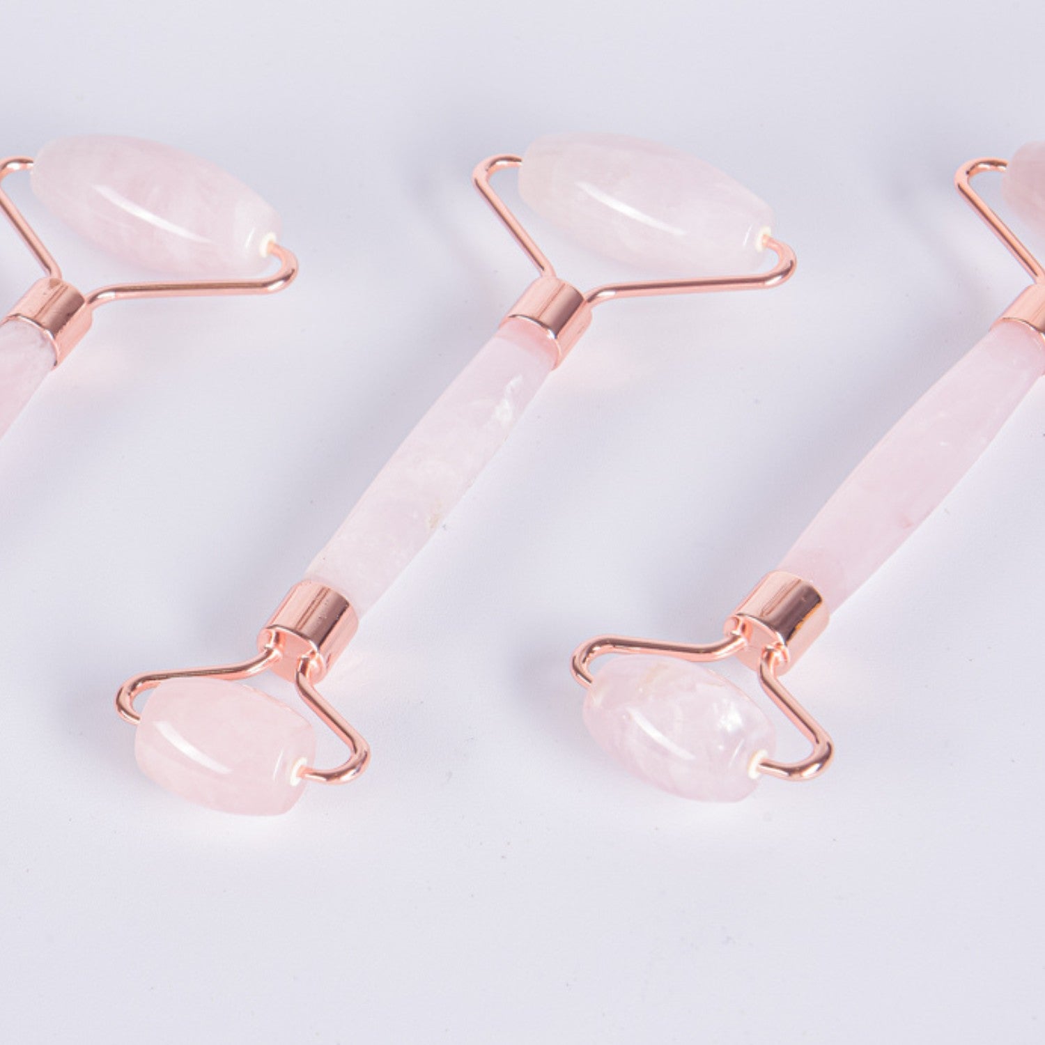 Detalle de masajeadores faciales de Cuarzo Rosa natural con acabados en metal color cobre (Rose Gold). Primer plano de los cabezales dobles de piedra auténtica.