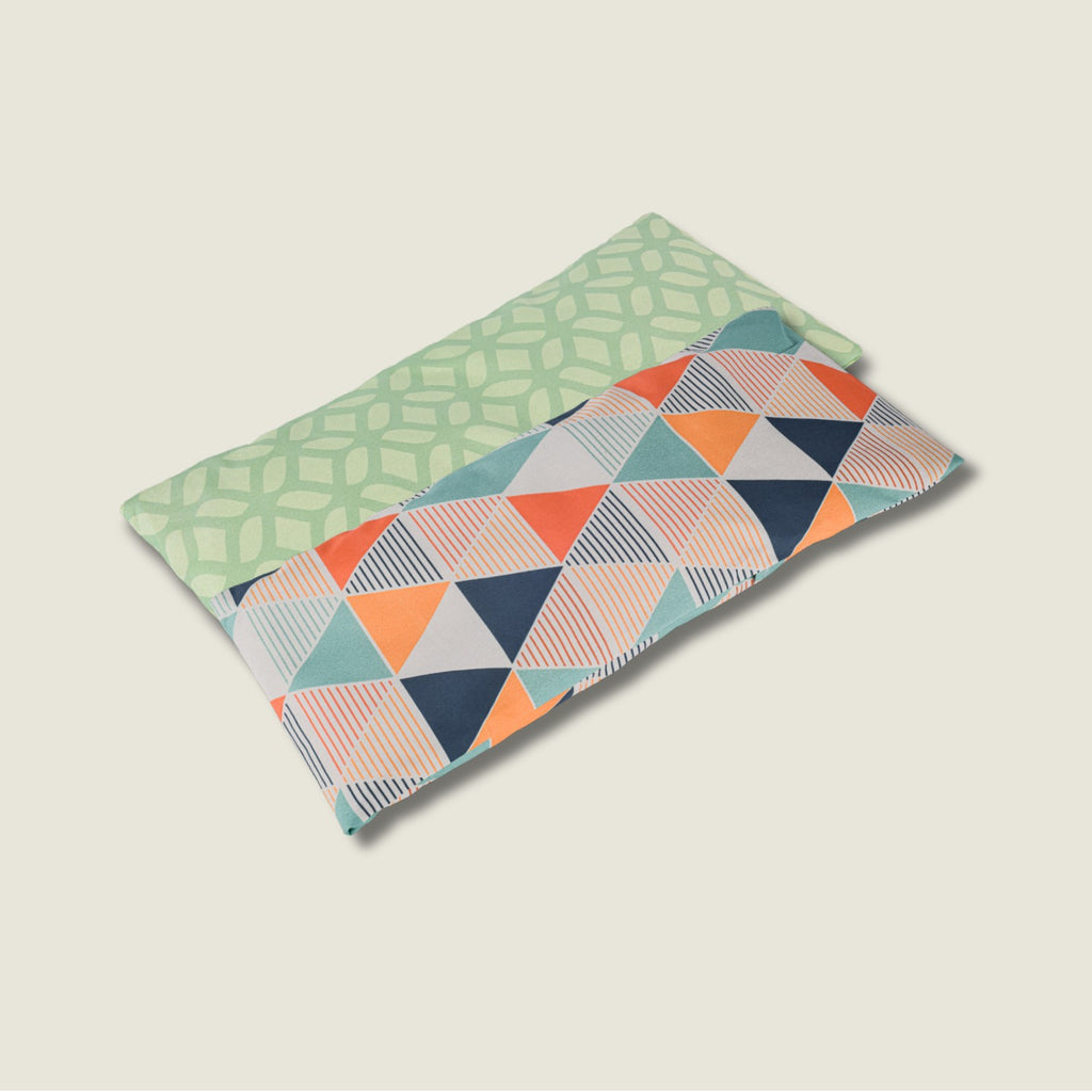 Dos sacos térmicos terapéuticos de semillas y lavanda. Modelos con funda lavable en estampado geométrico verde y triángulos naranjas.