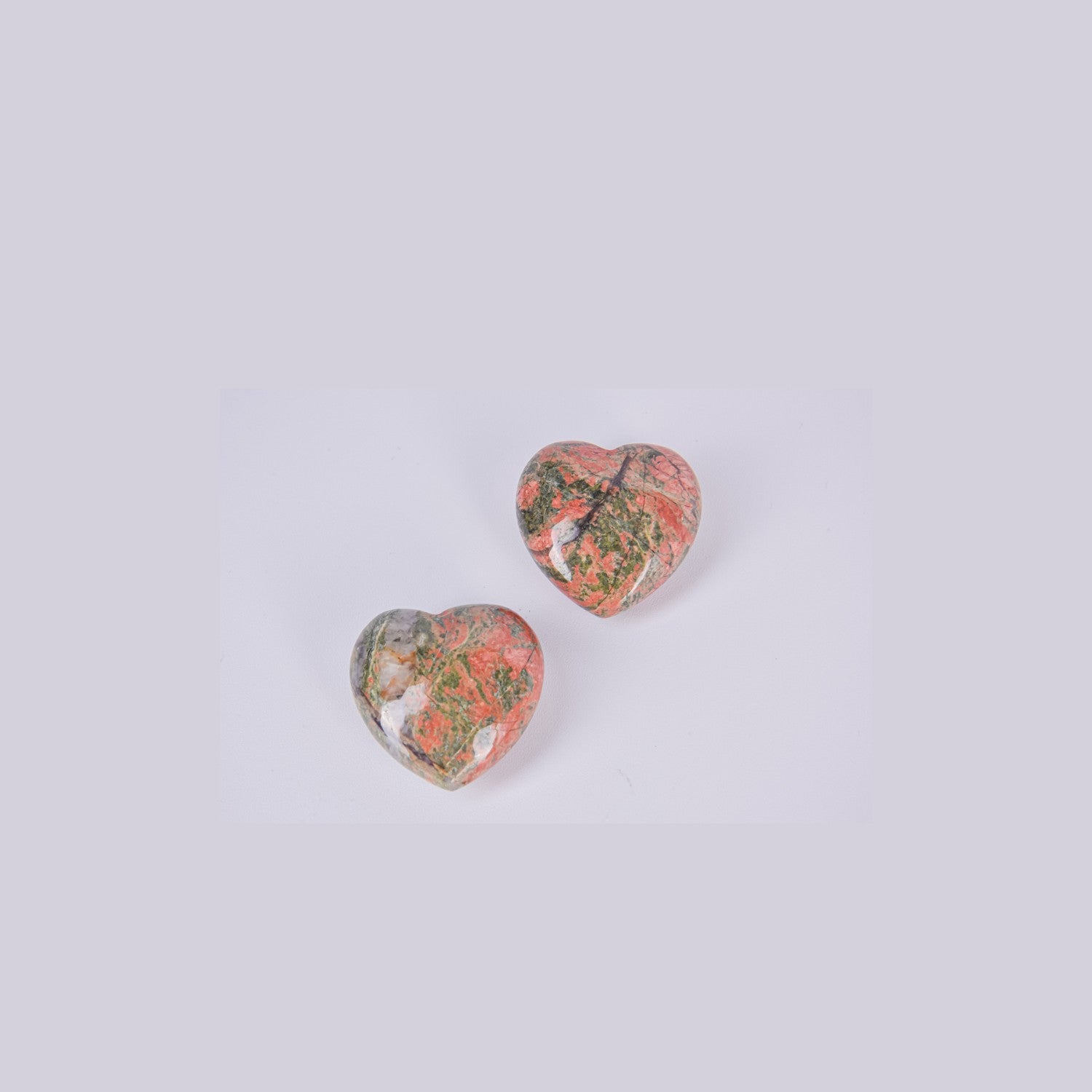 Dos corazones de piedra Unakita mostrando la variedad de patrones naturales únicos, mezclando tonos verde epidota y rosa feldespato.